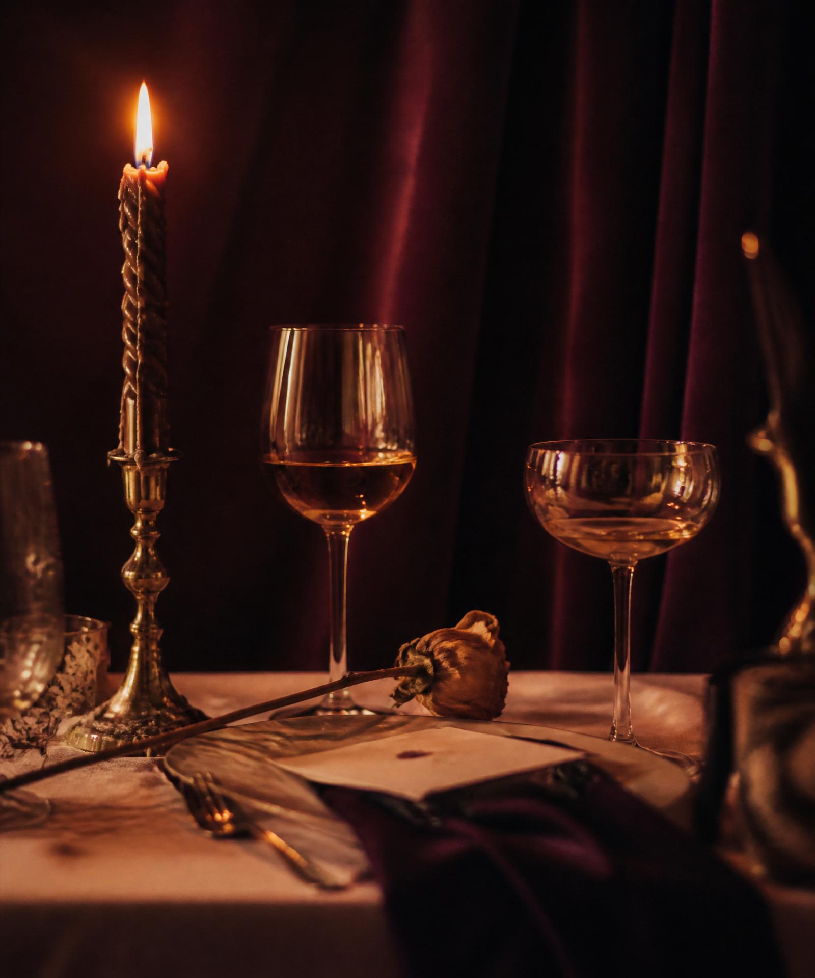 Candlelit table with two wine glasses and a dried rose against deep aubergine velvet